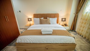 A neatly made bed with a wooden headboard, two bedside lamps, and a pair of white towels on the bed. - NIAMEY MALL & RESIDENCE (Niamey)