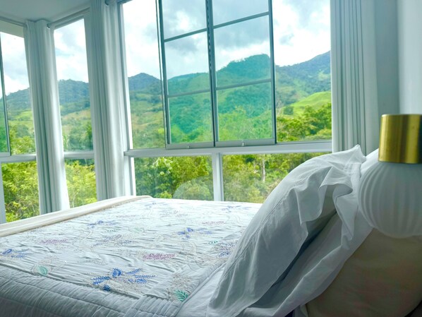 A bedroom with a large window offering a view of green hills. - Albergue Gstir (Pozuzo)