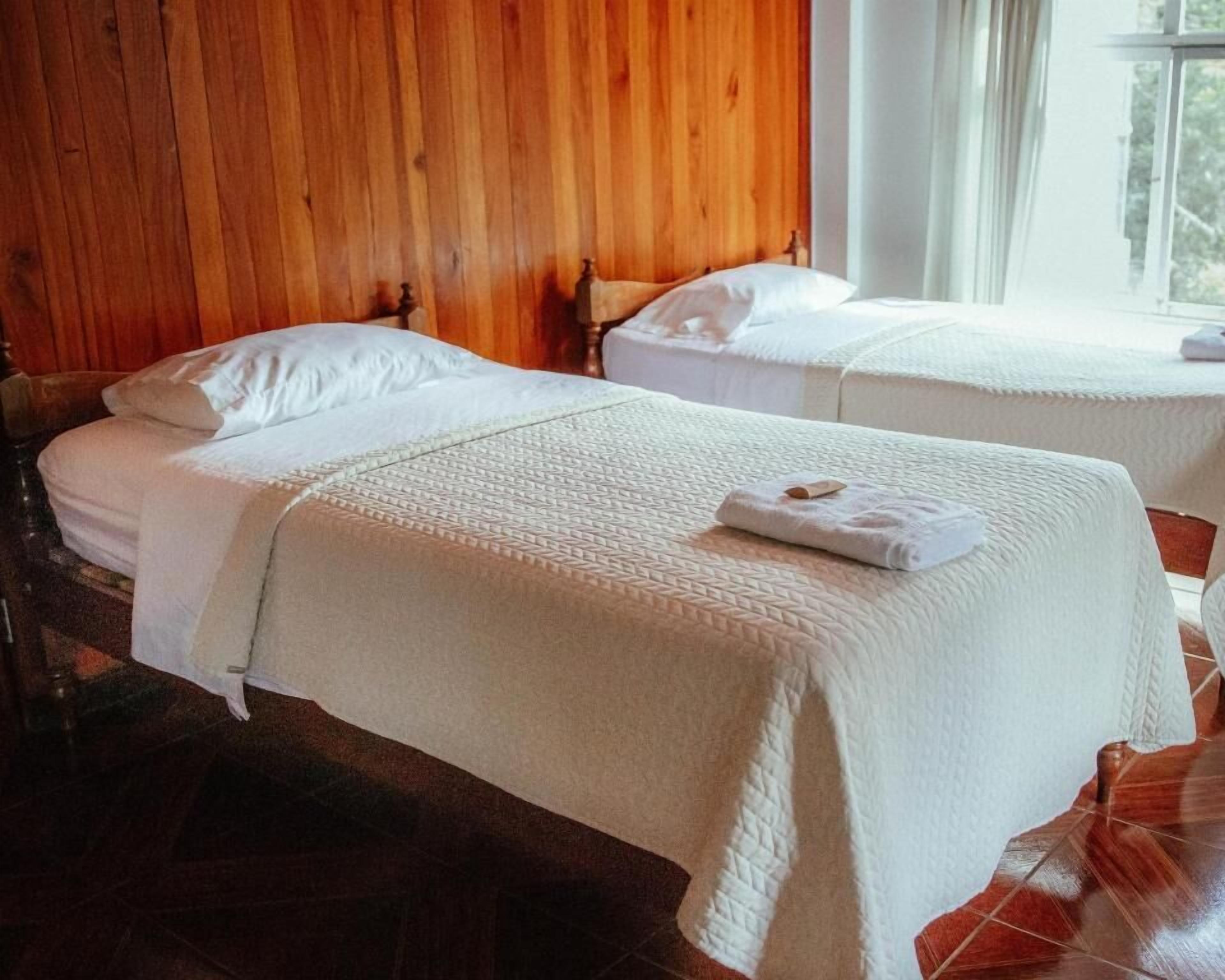 Habitación de hotel con dos camas, paneles de madera en las paredes y una ventana con cortinas.
