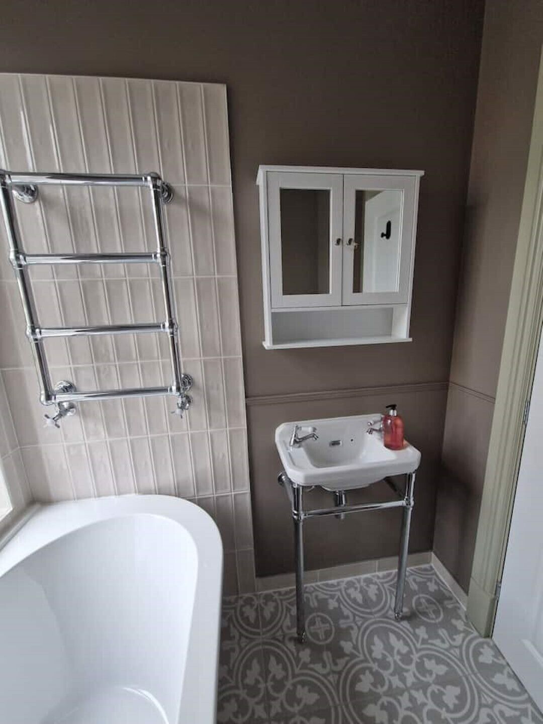 Een badkamer met een witte badkuip, een handdoekhouder, een wastafel met een zeepdispenser en een spiegelkast.
