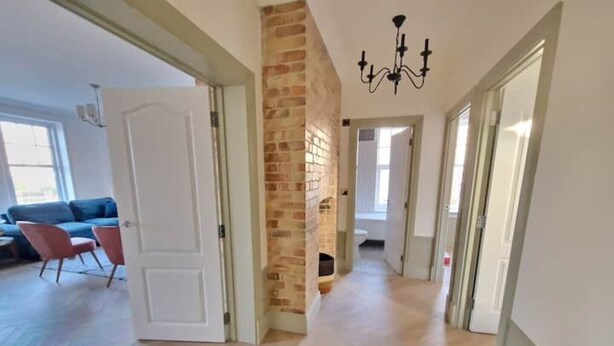 Un hall d’entrée spacieux, doté d’un parquet à motifs en chevrons, d’un mur en briques apparentes et d’un lustre.