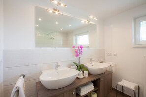 Une salle de bain moderne avec deux lavabos, un grand miroir et une petite fenêtre.