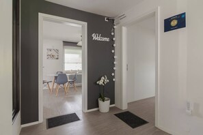 Un interior modern amb un cartell que diu 'Welcome', una orquídia en test i una zona de menjador amb cadires i taula.