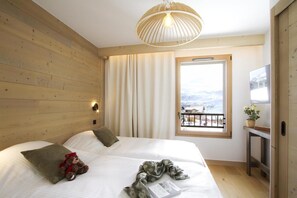 A hotel room with a wooden headboard, a large bed with white bedding, a bedside lamp, a window with a view of a snowy landscape, and a television on a wooden stand.