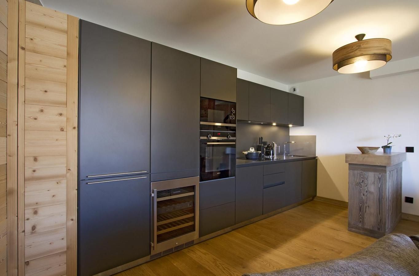 A modern kitchen with built-in appliances, a wooden accent wall, and a pendant light fixture.