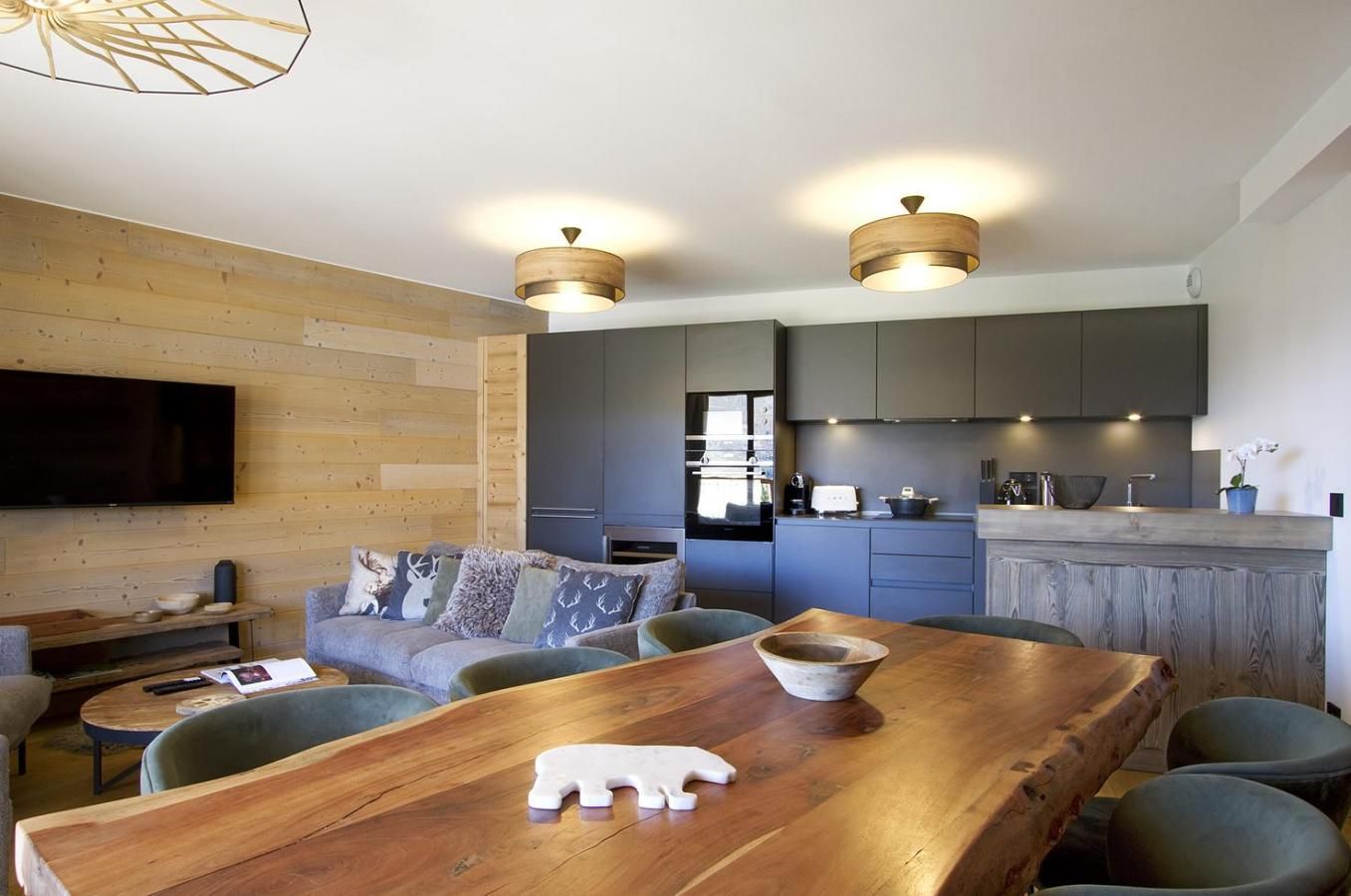 Una cocina moderna con armarios oscuros, una mesa de comedor de madera y un televisor de pantalla plana montado en la pared.