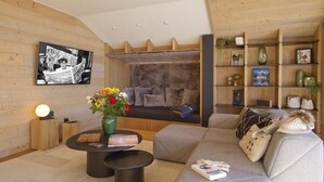 Un salon chaleureux avec un canapé, une table basse et une cheminée. On y trouve une bibliothèque remplie de livres et d’objets décoratifs.