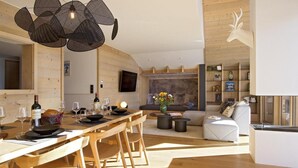 Un espace de repas moderne avec une table en bois dressée pour un repas, un canapé agrémenté d’un vase à motifs floraux et une décoration représentant une tête de cerf au mur.