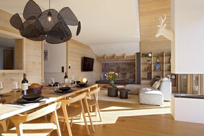 Uma zona de refeições moderna com uma mesa de madeira posta para uma refeição, um sofá com um vaso de flores e uma decoração de cabeça de veado na parede.