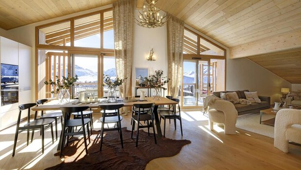 A spacious living room with a large wooden ceiling, a dining area with a table and chairs, and a sofa.