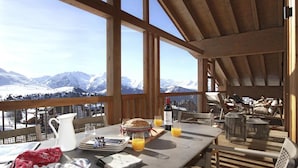 A dining area with a table set for breakfast, a view of snow-capped mountains, and a wooden interior.