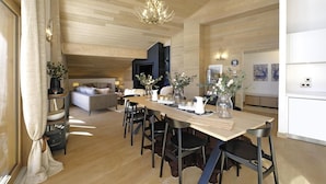 A spacious living area with a wooden ceiling, a dining table set with chairs, and a modern chandelier.