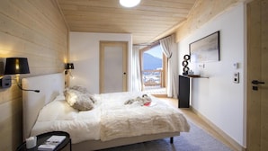A bedroom with a bed, a bedside table, a lamp, a window with a view, and a door.