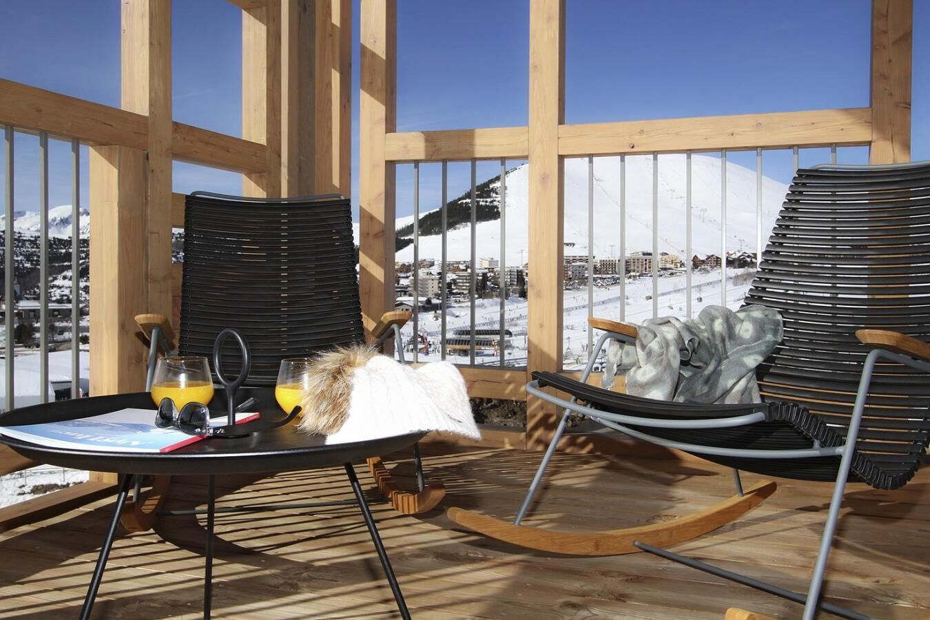 A wooden deck with two rocking chairs, a table with a glass of orange juice, and a glass of water.