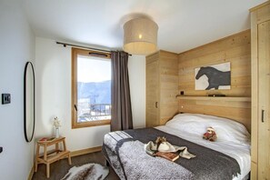 A bedroom with a large window, wooden headboard, and a view of mountains. - 10m from ski slopes, 5th floor, fitness, swimming pool, sauna, hammam, balcony, tv, ski locker, 70m² (Huez)