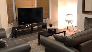 Un salon moderne avec un téléviseur à écran plat, des canapés sombres et une table basse.
