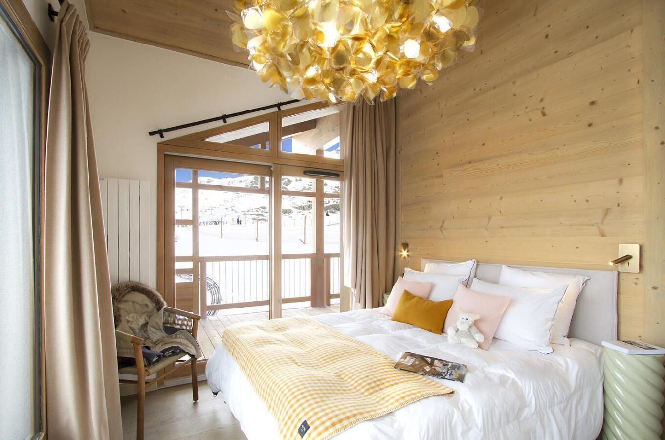 A bedroom with a bed, a window with curtains, a wooden ceiling, and a view of the outside.