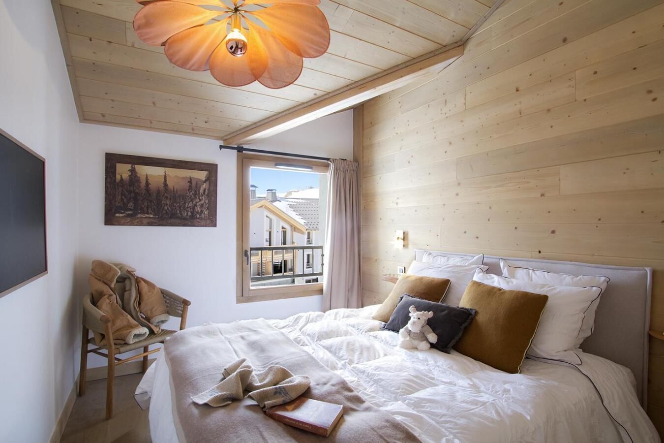 Quarto com cama, uma cadeira, um quadro e janela com vista para edifícios.