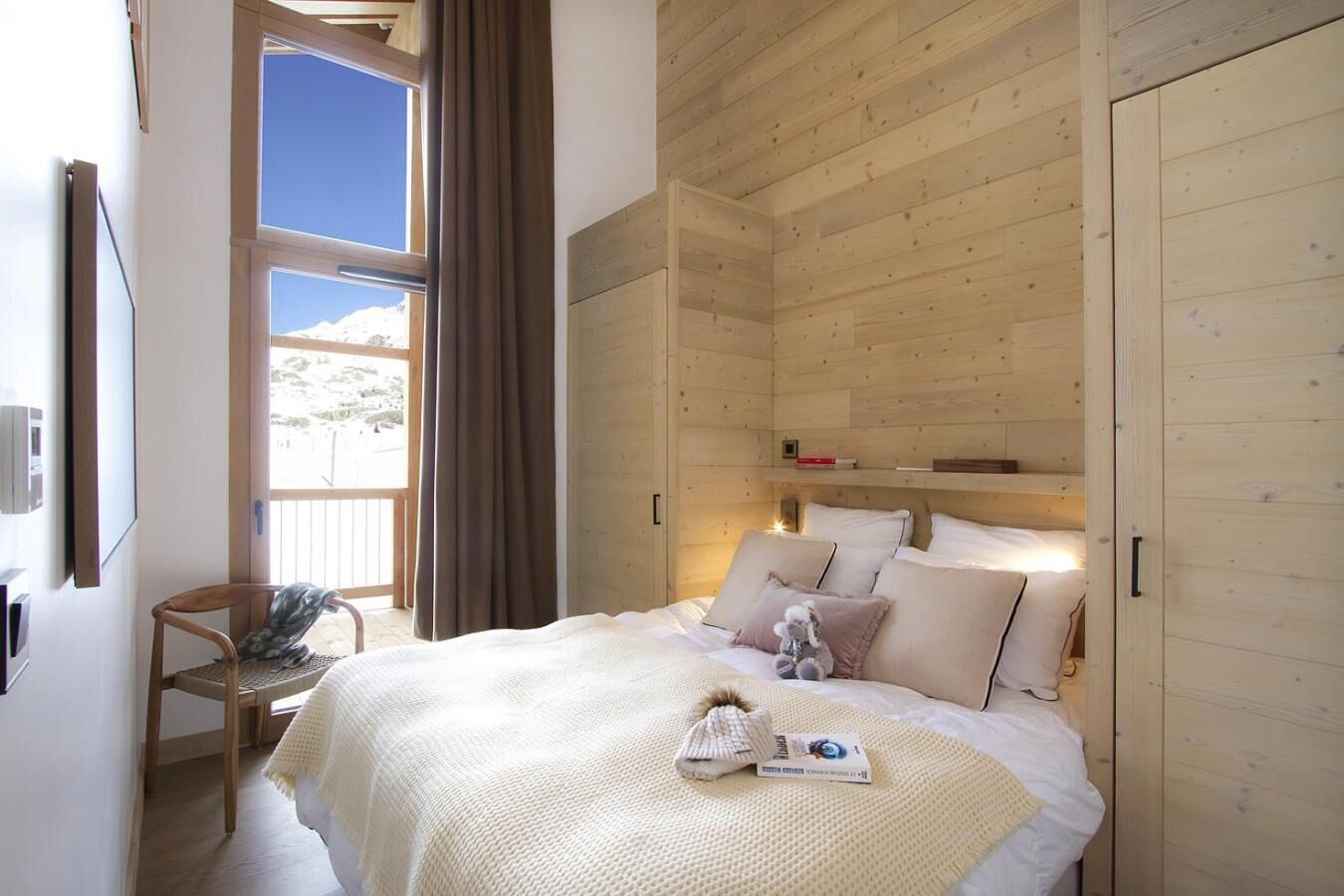 Een knus slaapkamer met een groot bed, houten wanden, een raam met gordijnen en een stoel.