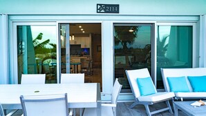 L’entrée d’un hôtel, avec une enseigne indiquant le numéro « 2114 », un espace patio doté de mobilier blanc et une vue sur l’intérieur à travers des portes vitrées.