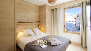 Une chambre à coucher comprenant un lit, une armoire en bois, une étagère, une lampe suspendue et une fenêtre donnant sur les montagnes.