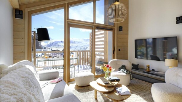 Ein gemütliches Wohnzimmer mit einem großen Fenster, einem Flachbildfernseher und einer Holzbalkendecke.