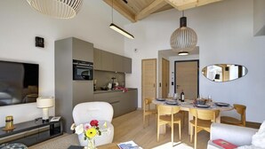 Ein modernes Wohnzimmer mit einer Couch, einem Esstisch mit Stühlen, einem Fernseher und einer Küchenzeile mit Schränken und Geräten.