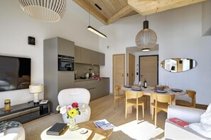 Ein modernes Wohnzimmer mit einer Couch, einem Esstisch mit Stühlen, einem Fernseher und einer Küchenzeile mit Schränken und Geräten.