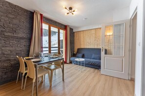 A room with a stone wall, wooden floor, a dining table with chairs, a sofa, and a small side table.