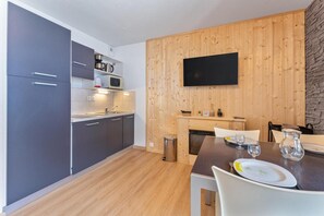 A modern kitchen with grey cabinets, a wooden wall-mounted TV, and a dining area with a table set for two.