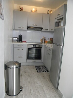 Una cocina compacta con refrigerador de acero inoxidable, horno empotrado y cafetera.