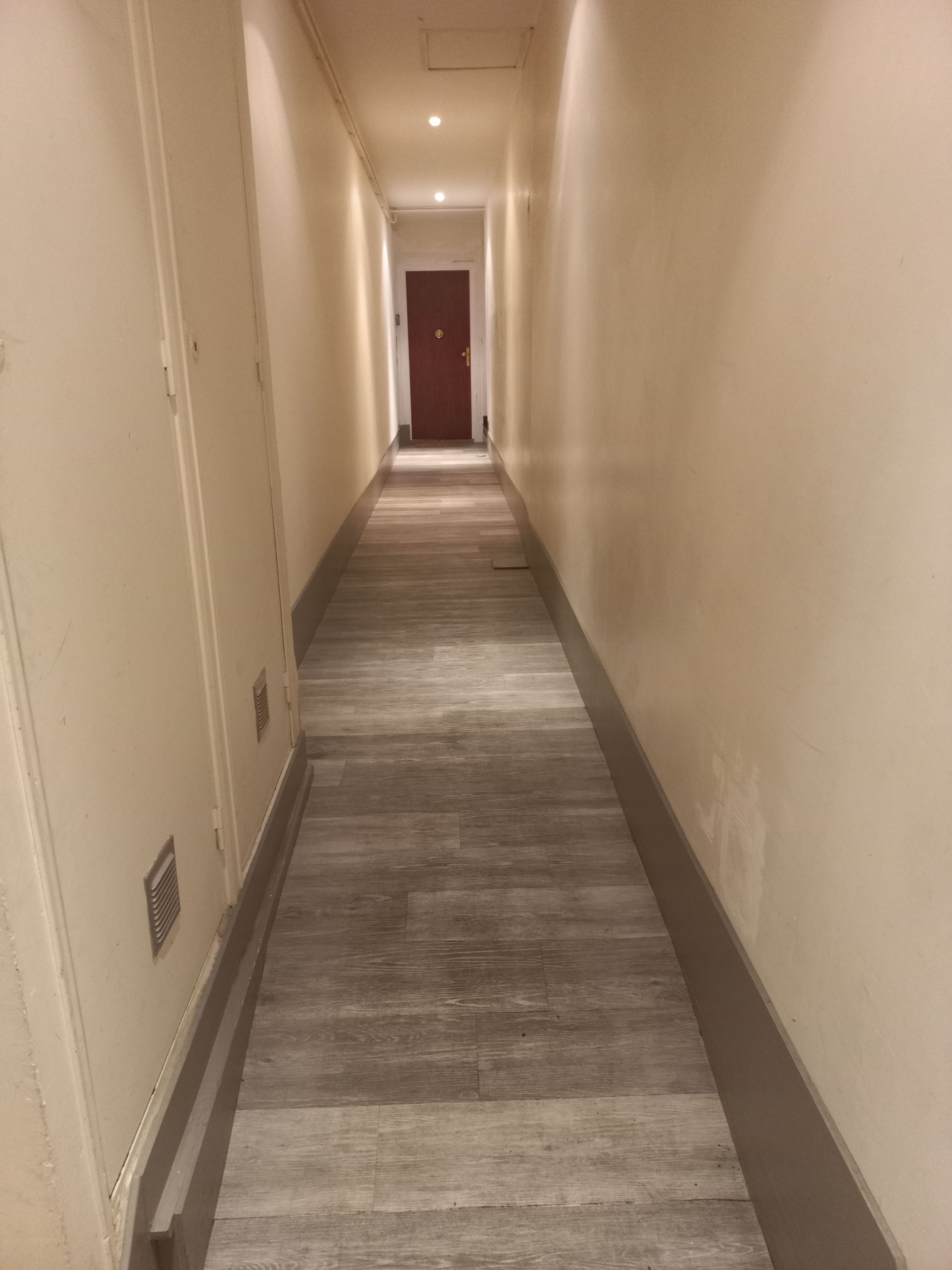 A long, narrow hallway with a wooden floor and beige walls.