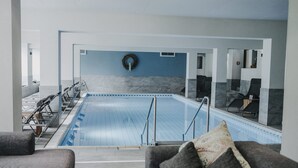 En moderne indendørs swimmingpool med frit udsyn over området, siddepladser og en vandinstallation på væggen.