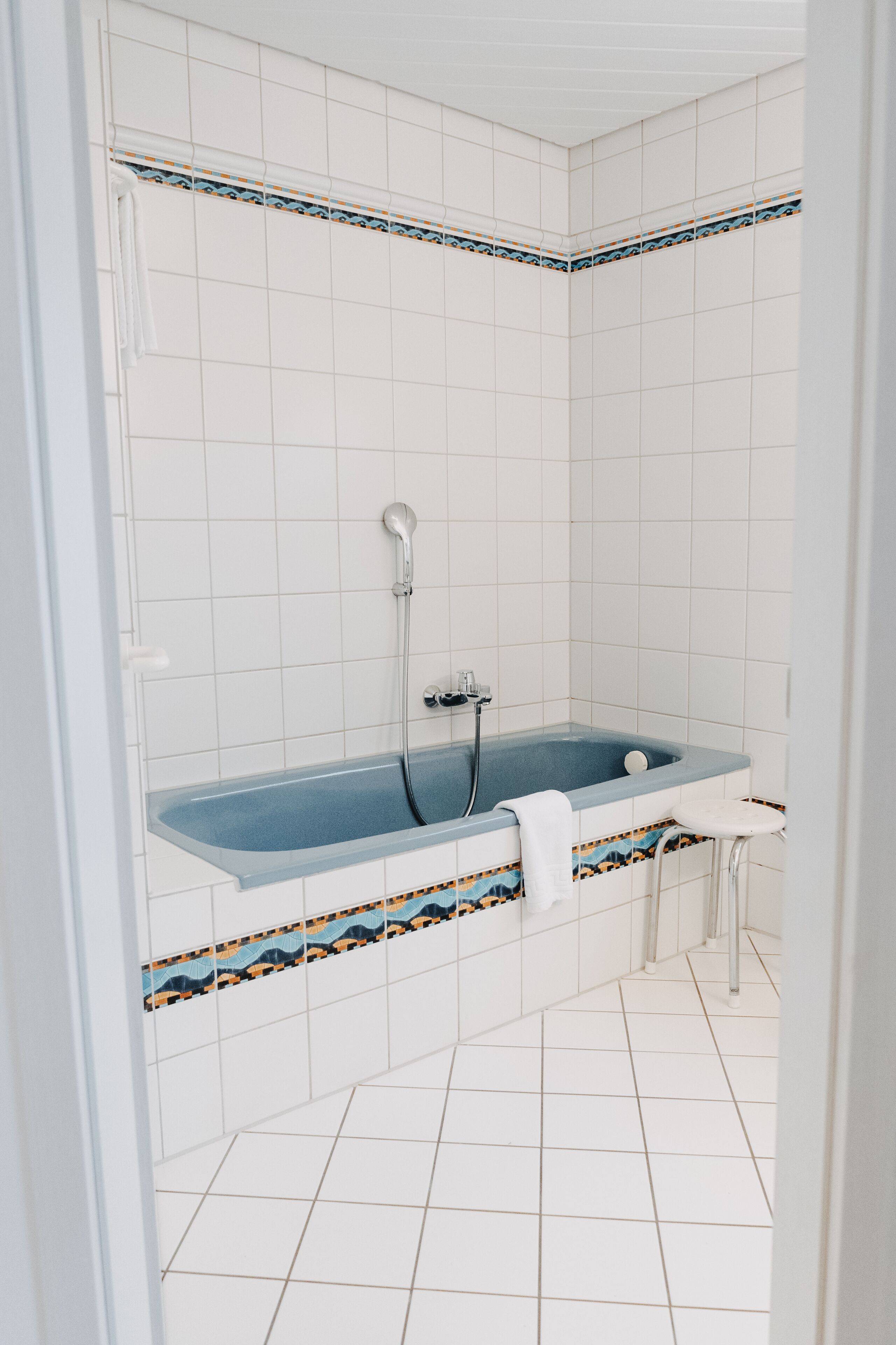 A bathroom with a bathtub, white tiled walls, and a patterned tile border.