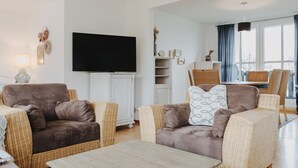 En moderne stue med et fladskærms-tv, fletmøbler og et spiseområde med bord og stole.