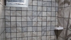 Un box de ducha con azulejos, un cabezal de ducha de mano y una pequeña ventana.