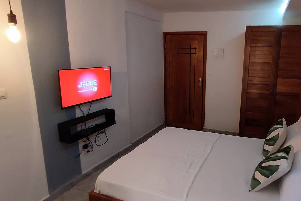 A bedroom with a bed, a TV mounted on the wall, and a wooden wardrobe.
