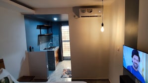 Una sala de estar con televisor, una cocina al fondo y una escalera que sube a otro nivel.