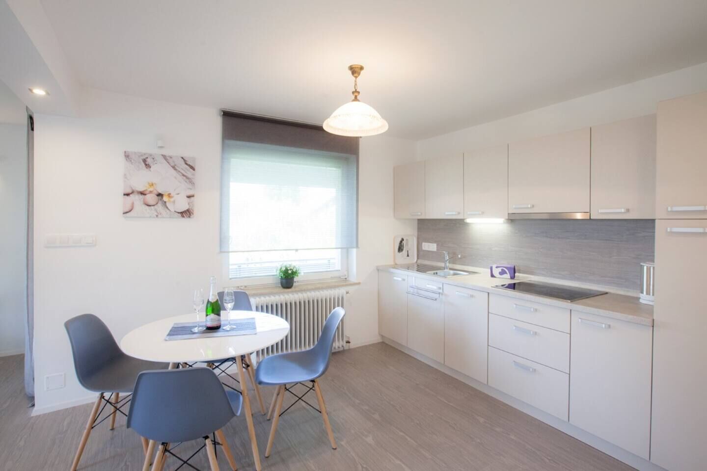 Une cuisine moderne avec des meubles blancs, une table à manger entourée de chaises bleues et une fenêtre équipée de stores.
