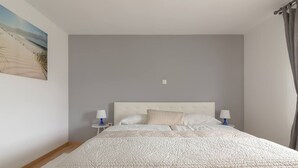 A bedroom with a large bed, two bedside tables with lamps, a painting of a beach scene, and a grey wall. - BLED - Flamingo apartment (Bled)