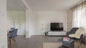 A modern living room with a flat-screen TV, a grey sofa, a dining area with chairs, and a small coffee table. - BLED - Flamingo apartment (Bled)