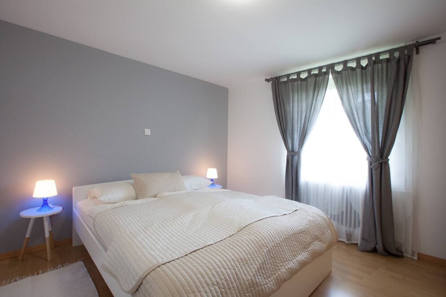 Een slaapkamer met een groot bed, twee bedlampen en een raam met gordijnen.