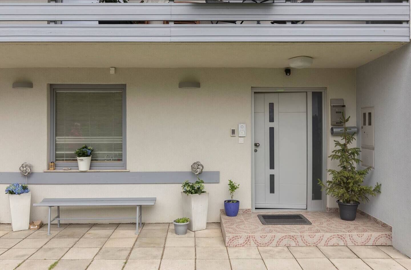 A modern building entrance with a bench, potted plants, and a door.