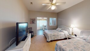 A bedroom with two beds, a TV, a ceiling fan, and a window. - Live the Golf Dream | River Creek Golf Condo in NC | RC 2002 (Sunset Beach)