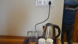 Un coin café comprenant une bouilloire, deux tasses et deux verres disposés sur un plateau, le tout branché à une prise de courant.