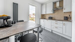 Una cucina moderna con mobili bianchi, zoccolo in piastrelle e una macchina da caffè.