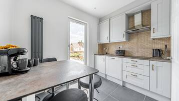 A modern kitchen with white cabinets, a tiled backsplash, and a coffee machine.