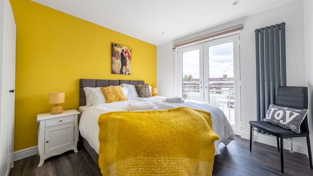 Una camera da letto con un letto, un comodino, una sedia, una finestra e un quadro appeso al muro.