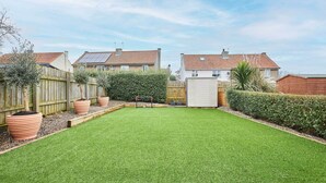 Ein gepflegter Garten mit Rasen, Holzzaun und Gartenhaus.