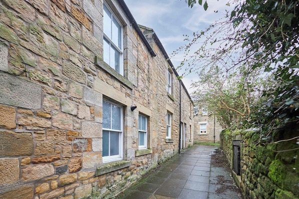 A narrow stone building with multiple windows and a paved walkway.